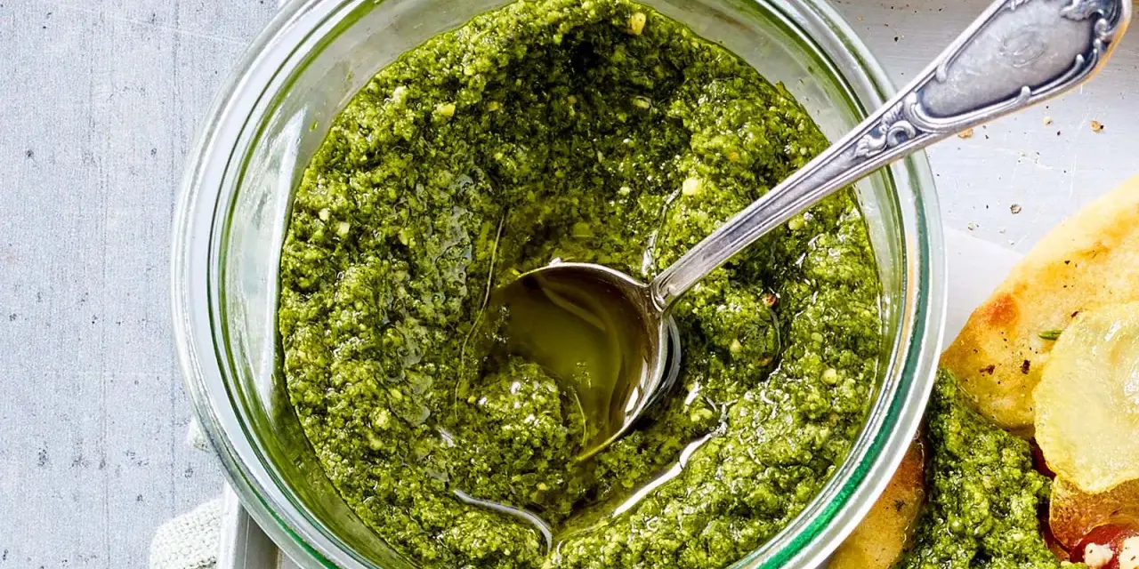 Frisches Basilikum Pesto in einem Glas, mit einem Löffel darin. Perfekt für Pasta oder Bruschetta.