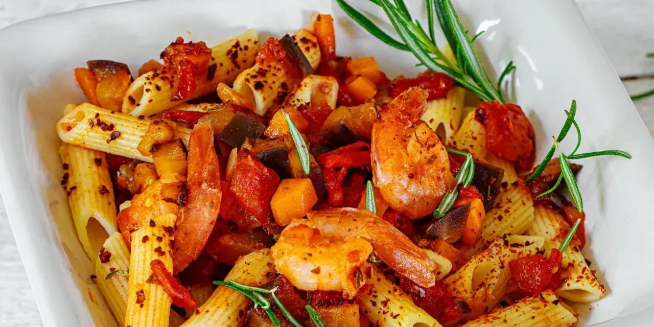 Penne-Nudeln mit Garnelen, Auberginen und Tomaten, garniert mit Rosmarin und Chiliflocken. Ein köstliches Gericht, das Lust auf mehr macht.