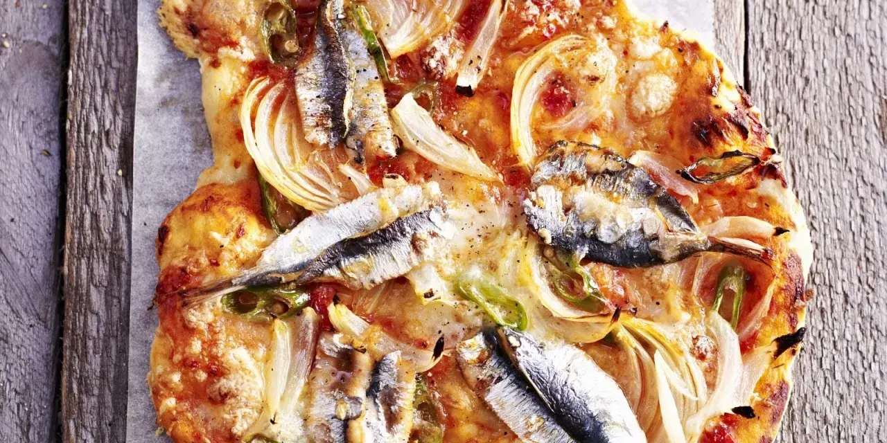 Eine rustikale Sardellen Pizza mit Zwiebeln und grünen Paprikastreifen, auf einem Holzbrett serviert.