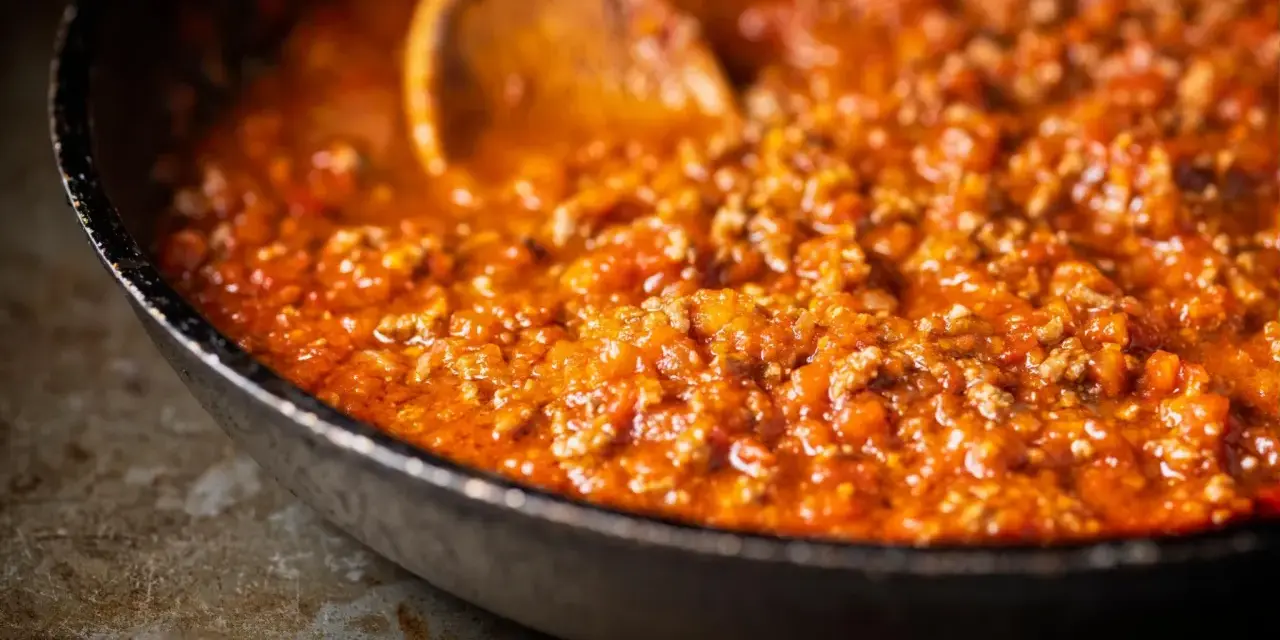 Herzhafte Bolognese-Sauce köchelt in einer Pfanne, die Zutaten für ein perfektes Pastagericht. Ein Holzlöffel rührt die köstliche Masse.