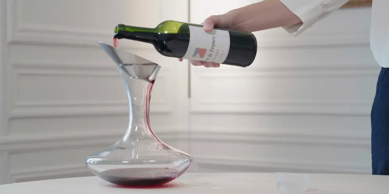 Roter Wein wird aus einer Flasche in einen Dekanter gegossen. Der Wein ist verkorkt und bereit zum Genießen.