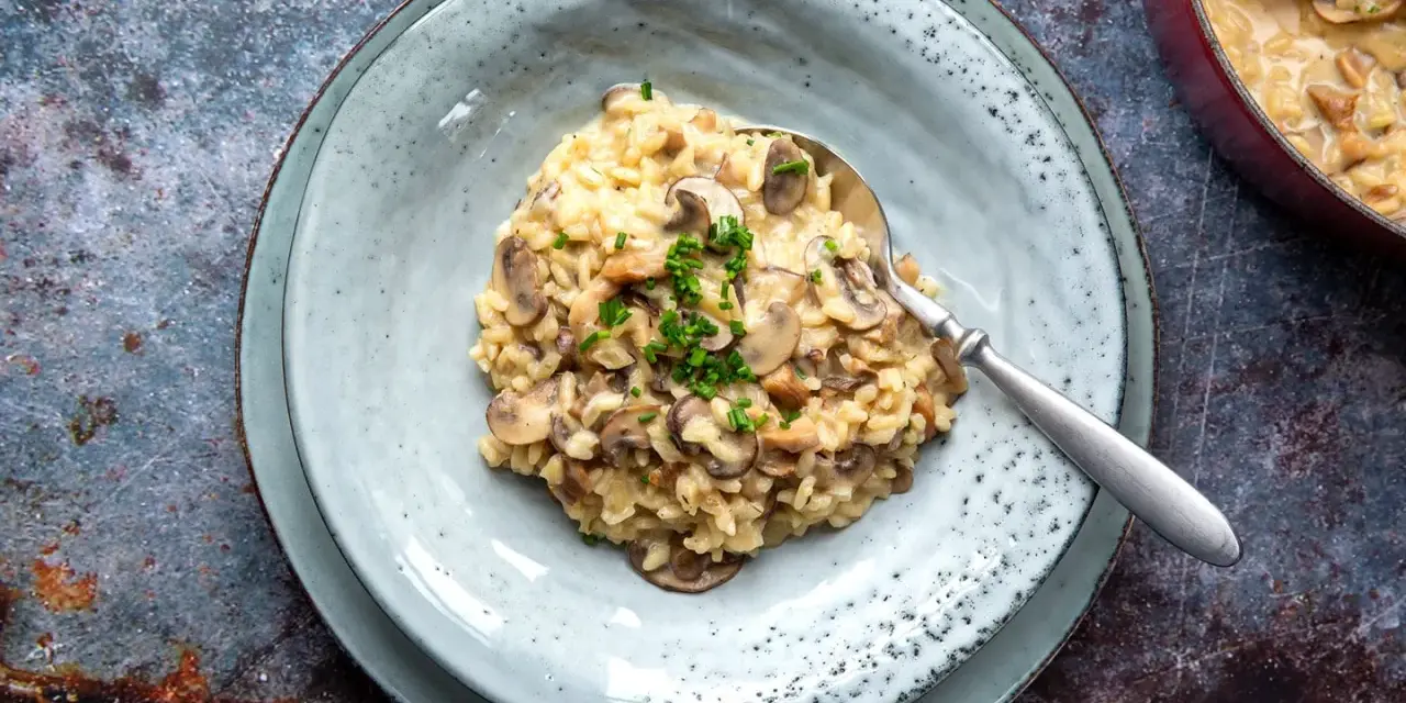 Cremiges Pilzrisotto, ein köstliches risotto rezept, garniert mit frischen Kräutern, auf einem Teller mit Löffel.