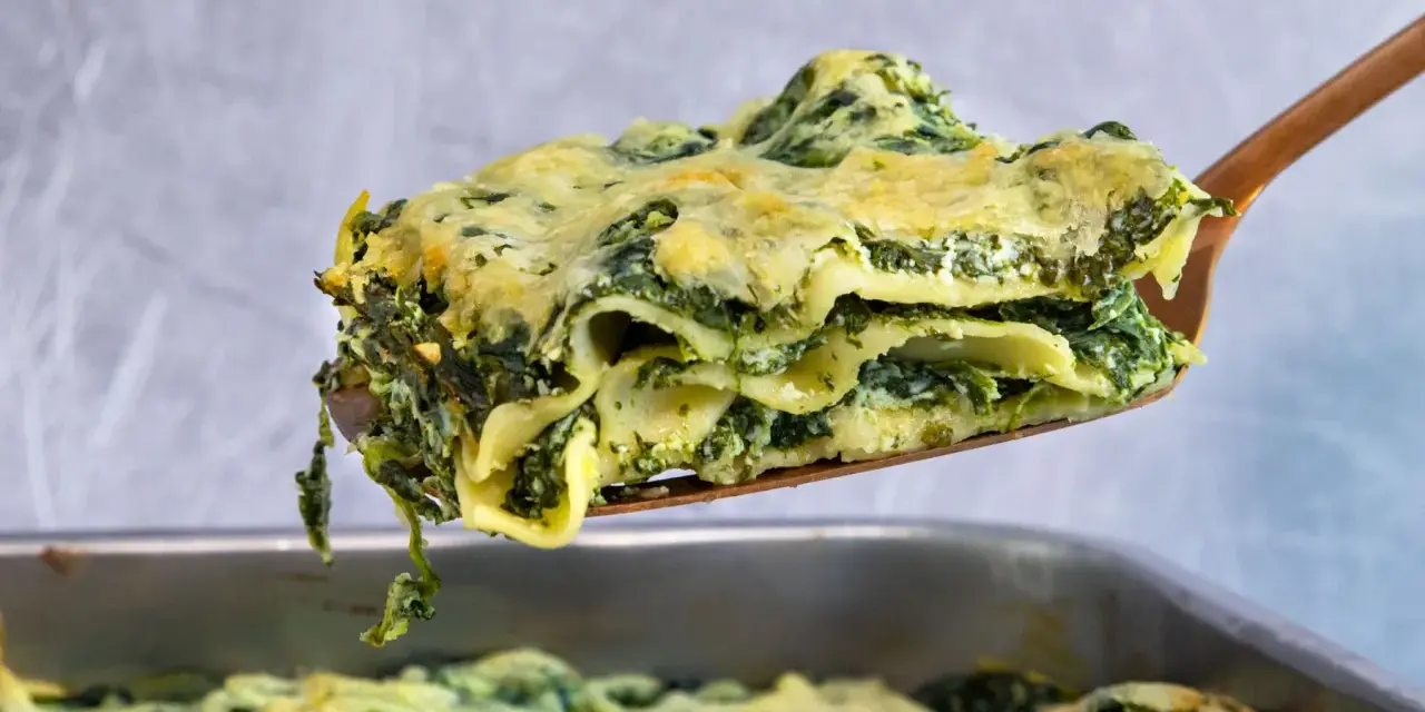 Ein Stück cremiger Ricotta Spinat Lasagne wird aus einer Auflaufform gehoben.