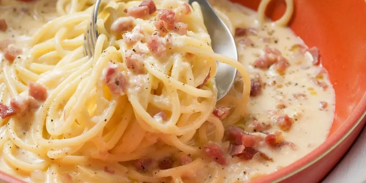 Cremige Pasta mit Ei und Speckwürfeln, ein klassisches italienisches Gericht, serviert in einer orangen Schüssel.