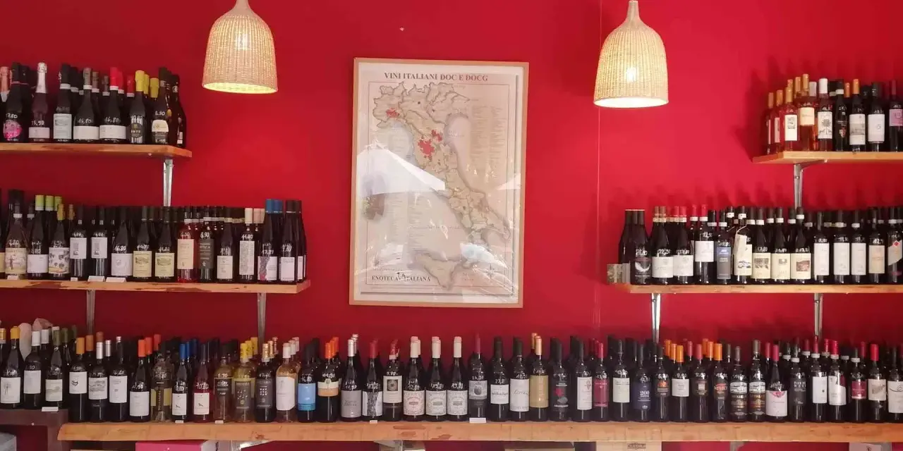 Regal voller italienischer Weinsorten vor roter Wand. Eine Karte Italiens mit Weinregionen hängt zentral.
