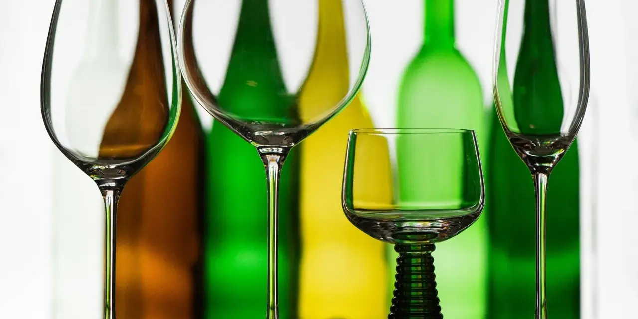 Leere Weingläser stehen vor bunten Flaschen. Perfekt, wenn man Wein kalt trinkt.