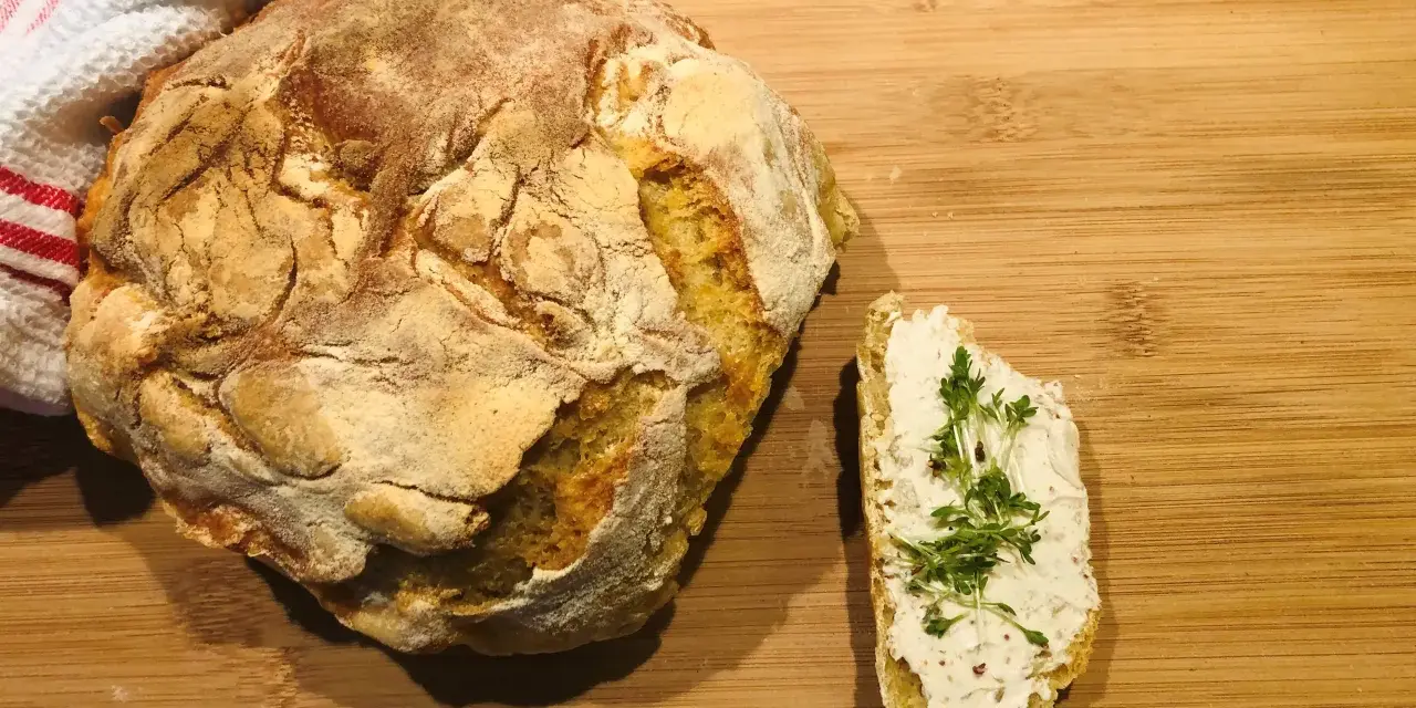 Ein rustikales, frisch gebackenes italienisches Brot Rezept, das genial einfach ist. Daneben ein Stück Brot mit Frischkäse und Kresse.