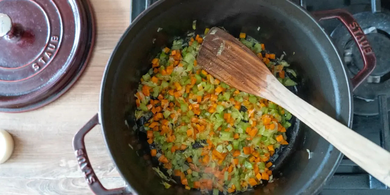 Würziges Sofrito Rezept: Karotten, Sellerie und Zwiebeln werden in einem gusseisernen Topf angedünstet.