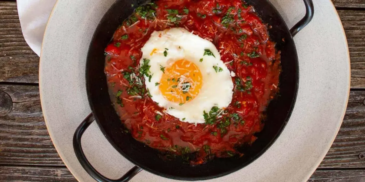 Ein Spiegelei ruht in einer würzigen Tomatensoße, garniert mit Kräutern und Käse. Ein Gericht, das an "uova in purgatorio" erinnert.