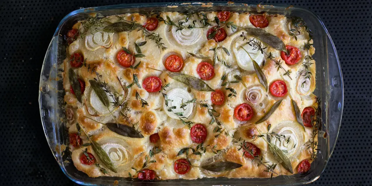 Frisch gebackene Focaccia mit Kirschtomaten, Zwiebelringen und Kräutern belegen.