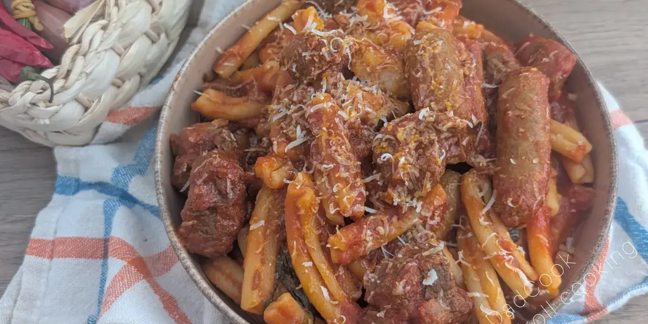 Herzhaftes Pasta Ragu mit Fleischstücken und geriebenem Käse, serviert in einer Schüssel auf einem karierten Tuch. Daneben ein Korb mit Knoblauch, Schalotten und Chilis.