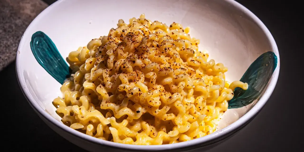 Cremige Pasta Alfredo, bestreut mit Gewürzen, in einer weißen Schüssel mit türkisfarbenen Akzenten.