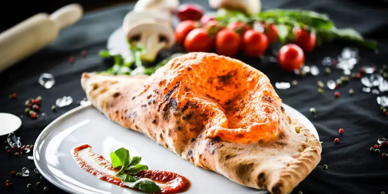 Ein goldbrauner, knuspriger Pizza Calzone mit geschmolzenem Käse und frischem Basilikum auf einem Teller.