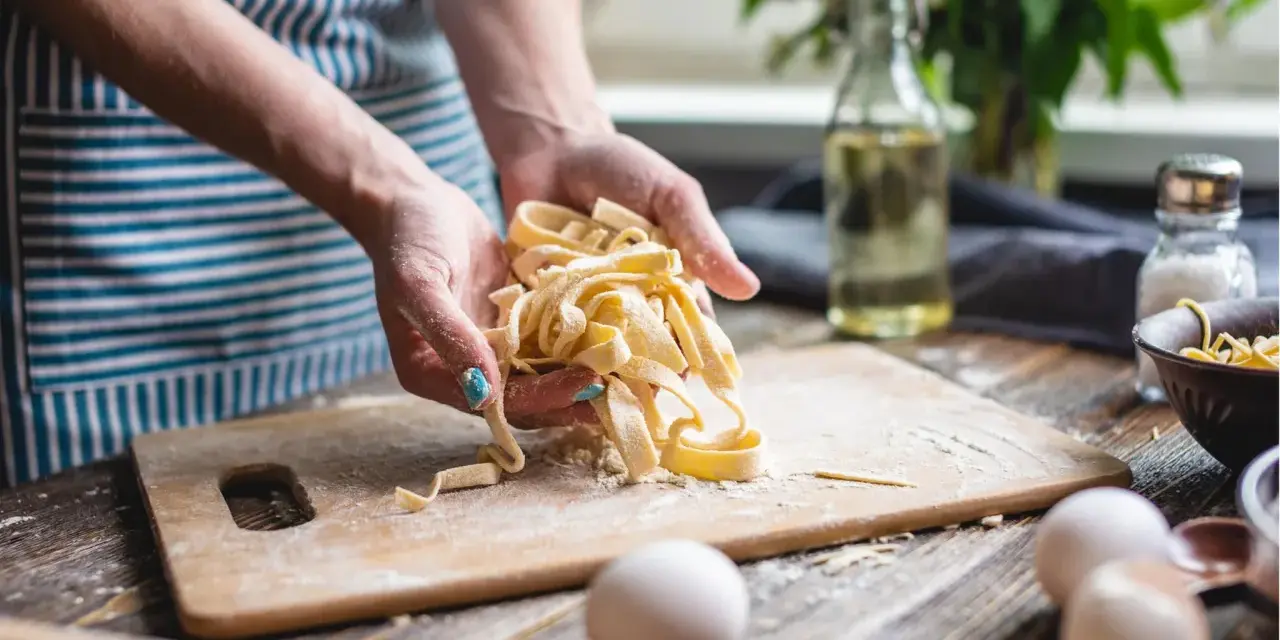 Frische Pasta aus dem perfekten pasta teig rezept. Hände halten die Bandnudeln, Mehl und Eier liegen bereit.