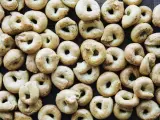 Viele goldbraune Taralli, die nach einem einfachen Taralli Rezept gebacken wurden, liegen dicht beieinander auf dunklem Holz.
