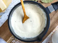 Cremige Béchamelsauce in einer Pfanne, bereit für Lasagne. Butter, Milch und Gewürze liegen daneben.