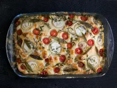 Frisch gebackene Focaccia mit Kirschtomaten, Zwiebelringen und Kräutern belegen.