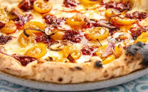 Eine köstliche Nduja Pizza mit geschmolzenem Käse, gelben Tomaten und roten Zwiebeln.