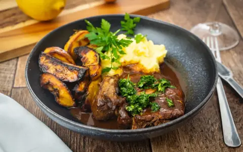 Ein Teller mit dem originalen Ossobuco-Rezept, dazu Kartoffelpüree und geröstete Kartoffelspalten.