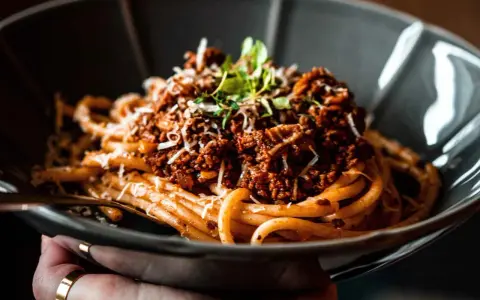 Eine Schüssel mit Pasta und original italienischer Tomatensauce mit Fleisch, garniert mit Parmesan und frischen Kräutern.