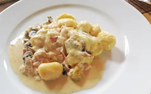 Gnocchi al forno mit cremiger Käsesauce, Pilzen und Schinken auf einem weißen Teller.