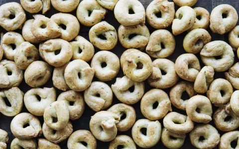 Viele goldbraune Taralli, die nach einem einfachen Taralli Rezept gebacken wurden, liegen dicht beieinander auf dunklem Holz.