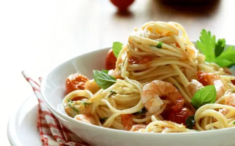Ein Teller mit köstlichen Spaghetti mit Garnelen, Kirschtomaten und frischem Basilikum, appetitlich angerichtet.