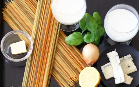 Zutaten für eine cremige Gorgonzola-Sauce: bunte Spaghetti, Butter, Zwiebel, Zitrone, Basilikum und Gorgonzola.