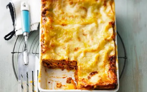 Eine frisch gebackene Lasagne al Ragu, goldbraun überbacken, wartet darauf, serviert zu werden. Ein Stück wurde bereits entnommen.