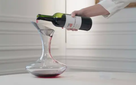 Roter Wein wird aus einer Flasche in einen Dekanter gegossen. Der Wein ist verkorkt und bereit zum Genießen.