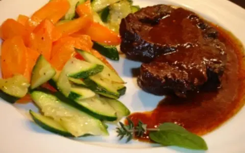Ossobuco vom Rind auf sizilianische Art, zart geschmort in dunkler Sauce, serviert mit Karotten und Zucchini.