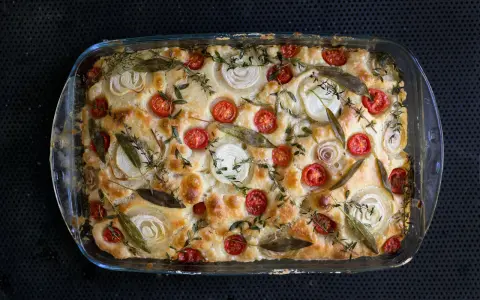 Frisch gebackene Focaccia mit Kirschtomaten, Zwiebelringen und Kräutern belegen.