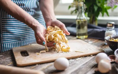 Frische Pasta aus dem perfekten pasta teig rezept. Hände halten die Bandnudeln, Mehl und Eier liegen bereit.
