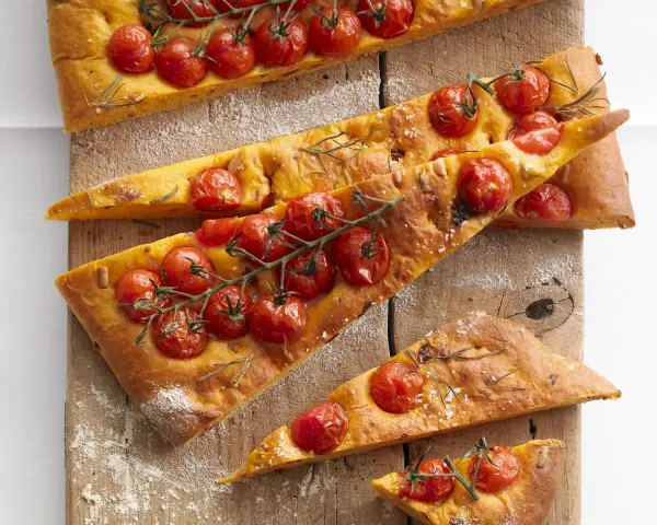 Saftige focaccia mit tomaten und Rosmarin, auf einem Holzbrett mit Mehl bestäubt.