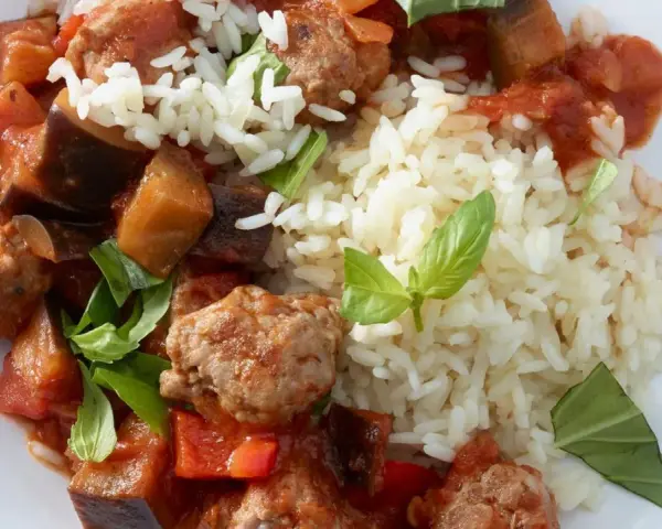 Herzhafte Salsiccia-Zubereitung in der Pfanne mit Auberginen, Paprika und Reis, garniert mit frischem Basilikum.
