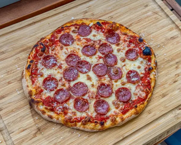 Eine köstliche Pizza Salami mit geschmolzenem Käse und knusprigem Rand liegt auf einem Holzbrett.