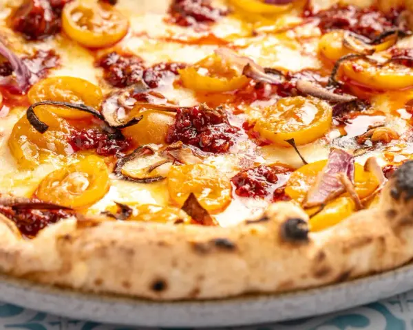 Eine köstliche Nduja Pizza mit geschmolzenem Käse, gelben Tomaten und roten Zwiebeln.
