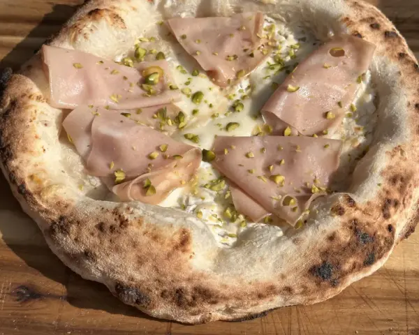 Frisch gebackener Pizzateig mit Mortadella und Pistazien. Ein Genuss, der das Pizzabacken zu einem Erlebnis macht.