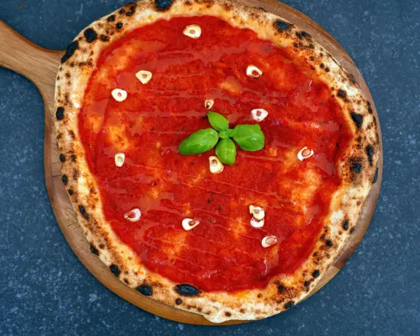 Eine klassische Pizza Marinara mit Tomatensauce, Knoblauch und frischem Basilikum auf einem Holzbrett.