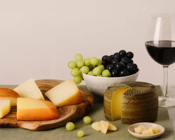 Käseplatte mit verschiedenen Käsesorten, Trauben und einem Glas Rotwein. Was bedeutet Primitivo bei Wein? Oft ein vollmundiger, fruchtiger Rotwein, der gut zu Käse passt.