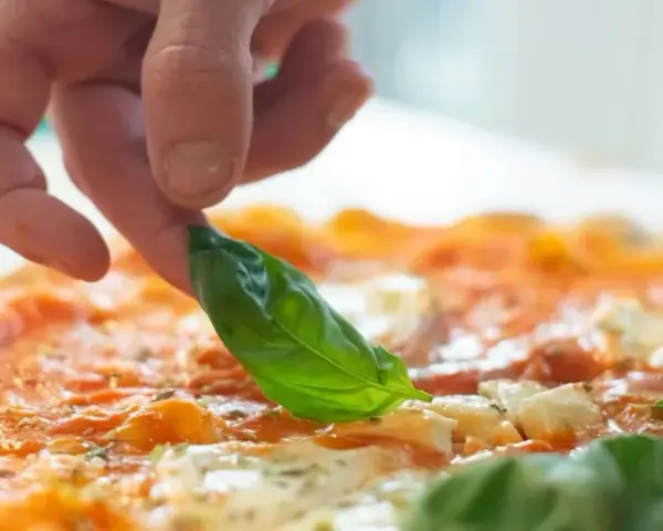 Eine Hand belegt eine Pizza mit frischem Basilikum. Die Pizza belegen reihenfolge ist wichtig für den perfekten Geschmack.