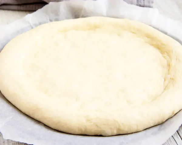 Ein runder, flacher Pizzaboden aus einem Pizzateig Rezept mit frischer Hefe, bereit für Belag und Backen.