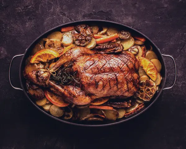 Brathähnchen mit Kartoffeln, Karotten, Orangen und Knoblauch. Ein Festmahl, das perfekt zu einem Glas Wein zu Ente passt.