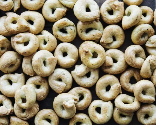 Viele goldbraune Taralli, die nach einem einfachen Taralli Rezept gebacken wurden, liegen dicht beieinander auf dunklem Holz.