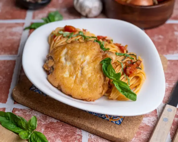 Ein paniertes Hähnchenfilet auf Spaghetti mit Tomatensoße und Basilikum. Ein Gericht, das an Piccata erinnert, aber ohne Zitrone.