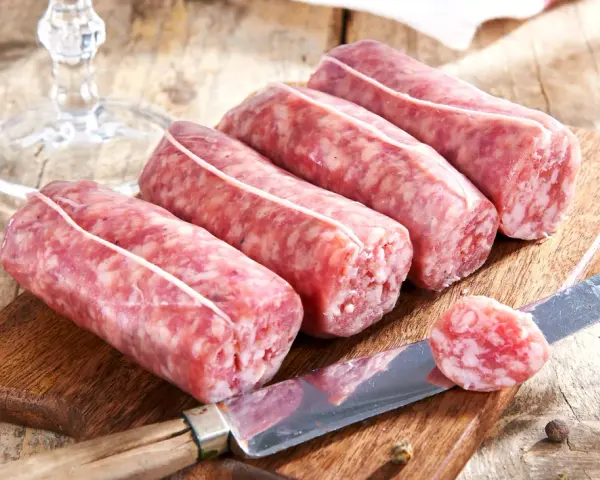 Frische Salsiccia zum Zubereiten liegen auf einem Holzbrett. Ein Messer mit einer Scheibe daneben deutet auf die Vorbereitung hin.
