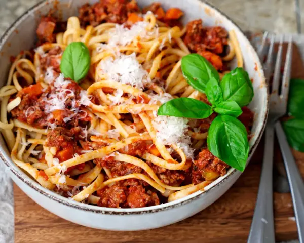 Eine Schüssel mit Linguine und einer herzhaften, **schnellen Bolognese**, garniert mit frischem Basilikum und Parmesan.