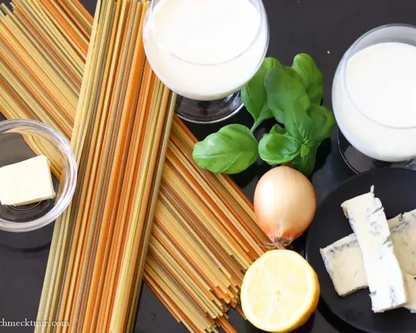 Zutaten für eine cremige Gorgonzola-Sauce: bunte Spaghetti, Butter, Zwiebel, Zitrone, Basilikum und Gorgonzola.