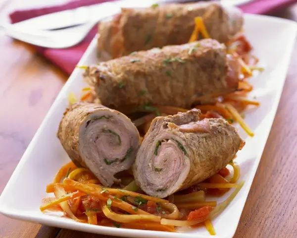 Drei köstliche kalbsrouladen italienisch auf einem Bett aus Gemüse. Eines ist aufgeschnitten und zeigt die saftige Füllung.