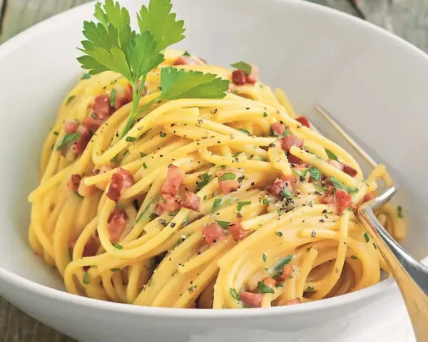 Spaghetti Carbonara mit knusprigem Schinken, garniert mit Petersilie und schwarzem Pfeffer, serviert in einer weißen Schüssel.